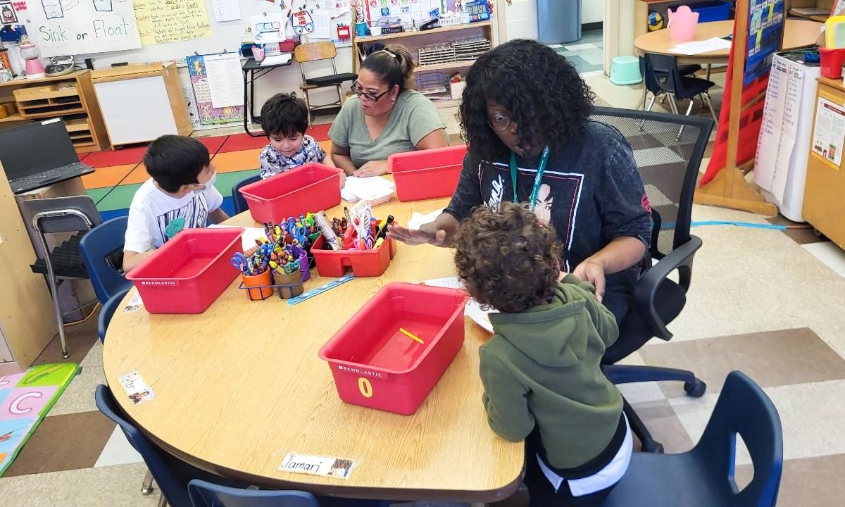 Kindergarteners work with two teachers around a circle table